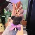 Rhinestone bear keychain detail view, featuring black crystal head, purple bow and gold ring. - Deep purple