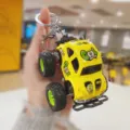 Detail view of a creative mini off-road car keychain with yellow body and big tires. - Yellow