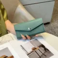 Elegante grüne Damen Geldbörse aus Leder in der Hand, mit feiner Textur und Klappendesign. - Grün