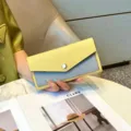 Close-up view of the dual-tone leather long wallet featuring an envelope flap and snap button. - Yellow and Gray Color-Block