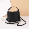 Detailed view of black leather shoulder bag with double handles and metal hardware. - Black