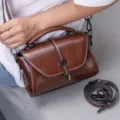 Close-up detail of retro brown oil wax leather shoulder bag with chic metal lock closure. - Coffee