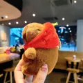 Cute plush capybara keychain with a red strawberry hat, soft bag pendant and keyring accessory. - Strawberry