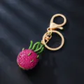 Close up detail shot of shiny rhinestone dragon fruit metal keychain with golden ring and clasp. - Dragon Fruit Style