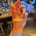 Close-up of cute mini oil lamp keychain with glowing night light feature and small bell pendant. - Orange