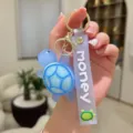 Detalle de llavero de tortuga azul, material de PVC suave con correa morada y anillo dorado. - Azul