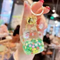 Detailed view of transparent liquid quicksand lucky cat keychain with glitter and bell. - Grass Green