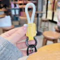 Detailaufnahme des geflochtenen Seil-Schlüsselanhängers mit gelbem Lederetikett und Metallring. - Weiß