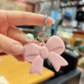 Pink acrylic bow keychain with pearl charm and silver clasp, cute detail accessory. - Pink