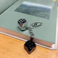 Close-up view of the double dice keychain with silver and black dice hanging on a book. - Silver and Black