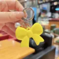 Detailed close-up of a cute yellow acrylic bow keychain with pearl pendant, stylish accessory. - Yellow
