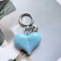 Close-up detail shot of light blue heart keychain, glossy alloy bag charm accessory. - Blue