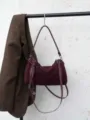 Detailansicht der burgunderroten Wildleder-Umhängetasche an einem Ständer mit Metallreißverschluss. - Ancorra Rot