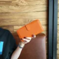 Orange pebbled leather long wallet featuring a secure flap closure and zip around design for women. - Orange