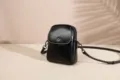 Black genuine leather vertical phone bag detail, compact crossbody design with stylish hardware. - Black