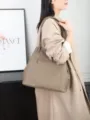 Detail shot of the taupe genuine leather shoulder tote bag worn by model, showing zipper pocket. - Small Size / Elephant Gray