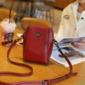 Detailansicht der roten Leder Umhängetasche für Handys auf Tisch mit schöner Metallblume. - Rot