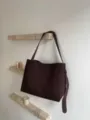 Detailansicht einer großen braunen Wildleder-Umhängetasche an einem minimalistischen Regal. - Klein / Kaffeebraun