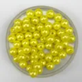 Close-up detail of glossy yellow ABS pearl beads in a clear tray for DIY jewelry making crafts. - Yellow