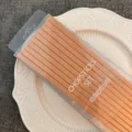 Vista dettagliata del set di bacchette in lega marrone chiaro in scatola di plastica trasparente. - Arancione