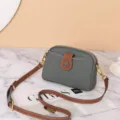 Grey and brown leather crossbody bag detail showcasing fine stitching, zipper and metal hardware. - Aqua