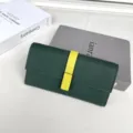 Dettaglio ravvicinato di portafoglio lungo donna verde scuro con cinturino giallo a contrasto. - Verde