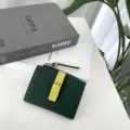 Detail view of dark green leather short wallet with contrast yellow strap, zipper pocket. - Green