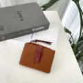 Detailed close-up of brown genuine leather bifold wallet with contrast red strap clasp and fine texture. - Brown