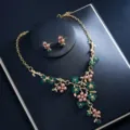 Exquisite gold-tone floral necklace and earrings detail featuring green crystals and pink pearls. - Green