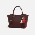 Bolso de mano de cuero burdeos para mujer con correa cruzada y elegantes dijes decorativos. - Rojo Oscuro