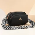 Bolso cruzado de cuero negro con elegante correa ancha tejida y herrajes dorados. - Negro