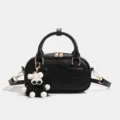 Bolso de mano tipo pillow de cuero negro con hermoso dije de peluche y bandolera chic. - Negro