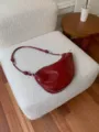 Red patent leather underarm saddle bag detail shot, stylish shoulder bag with metal accents. - Red