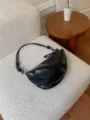 Detail view of a stylish black glossy shoulder bag with knotted strap on white chair. - Black