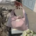 Close-up of sweet pink women handbag with bow detail and handle, elegant lifestyle outdoor scene. - 29x9x17cm / Pink