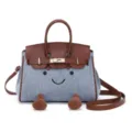 Cute denim patchwork handbag with smiley face design, featuring top handles and shoulder strap. - Denim Blue