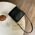 Close-up detail shot of the elegant black glossy shoulder bag on white table in daily life setup. - 18x8x17cm / Black