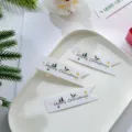 Close-up of minimalist white Christmas gift tags with Merry Christmas print and festive decor. - Leaf Style