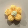 Gedetailleerde close-up van handgemaakte gehaakte wollen pofbloem, kledingaccessoire. - Geel