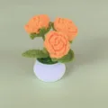 Handgemaakte gehaakte rozen potplant detail met oranje bloemen en groene bladeren in een witte pot. - Oranje