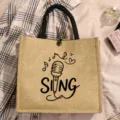 Detailed close-up view of a minimalist jute tote bag featuring a microphone sketch and SING slogan. - Style 7