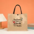 Vista dettagliata della borsa in iuta con stampa di testo, su una scrivania e sfondo caldo. - Stile I Piccoli Umani non mi Spaventano (6278935766198)