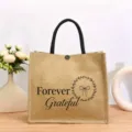 Nahaufnahme der Jute-Tragetasche mit Forever Grateful Aufdruck und schwarzen Griffen. - Botanischer Druck Stil Zwei