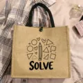 Detailed close-up view of a chic burlap tote bag featuring cute pencil print and solve text design. - Style 2