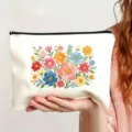 Detailansicht des weißen Canvas-Kosmetikbeutels mit bunter Blumenstickerei und schwarzem Reißverschluss. - Stil 13