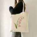 Detailaufnahme einer beigen Segeltuchtasche mit pinkem Lilienmotiv, ideal für Alltag und Reisen. - Maiglöckchen Blumen (3) / 35x40cm