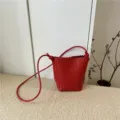 Dettaglio borsa secchiello in pelle intrecciata rossa, con elegante tracolla a nodo e trama raffinata. - Rosso