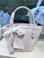 Dettaglio borsa a mano trapuntata rosa con elegante manico intrecciato, nastro floreale e ciondolo. - Rosa