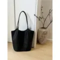 Dettaglio borsa shopper intrecciata in pelle nera minimalista, elegante contesto in legno. - Nero