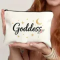 Nahaufnahme der weißen Kosmetiktasche mit Goddess-Schriftzug und goldenen Sternen. - Göttin Stil